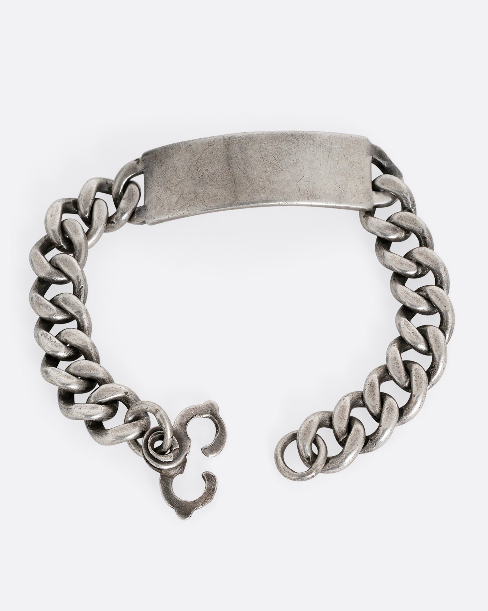 A silver cable chain ID bracelet with "A.R. Warren" in curling script  engraved on the inside of its name tag. Shown open from the front.