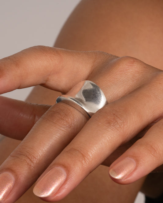 A silver ring with a fluid concave silhouette. Shown from the front on a hand.