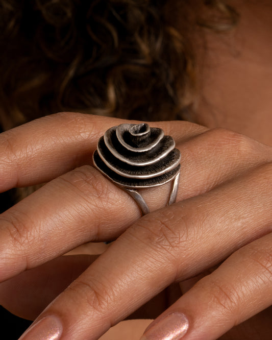 A silver ring with a coiling swirl on top and open shoulders. Shown from the side on a person.