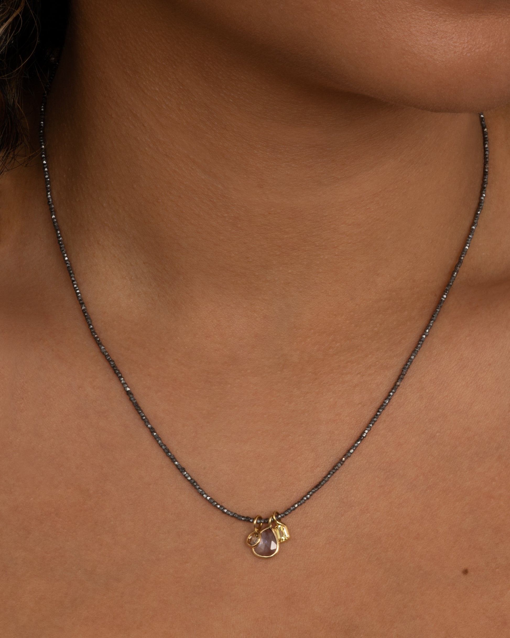 A necklace with oxidized silver Hill Tribe beads and a cluster of blue and green sapphires and a rose cut diamond. Shown from the front on a person.