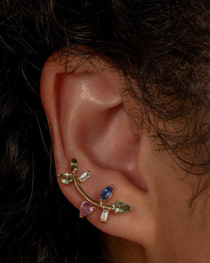 This elegant 14k gold stud, dotted with blue and green gemstones, reminds us of an olive branch. Shown worn in an ear.