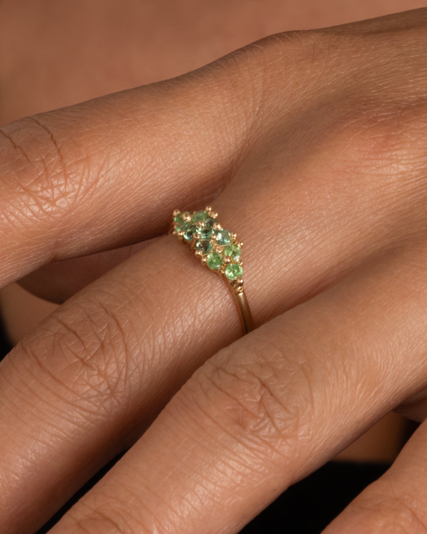 A yellow gold ring with a cluster of eleven green sapphires and tsavorite. Shown worn on hand.