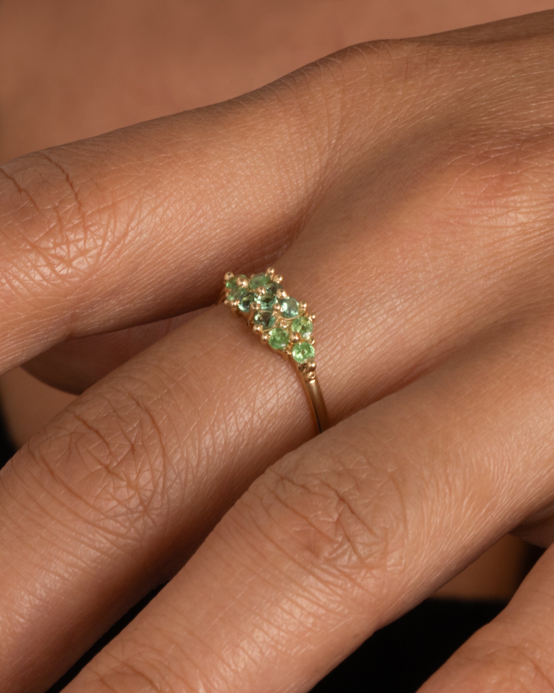 A yellow gold ring with a cluster of eleven green sapphires and tsavorite. Shown worn on hand.