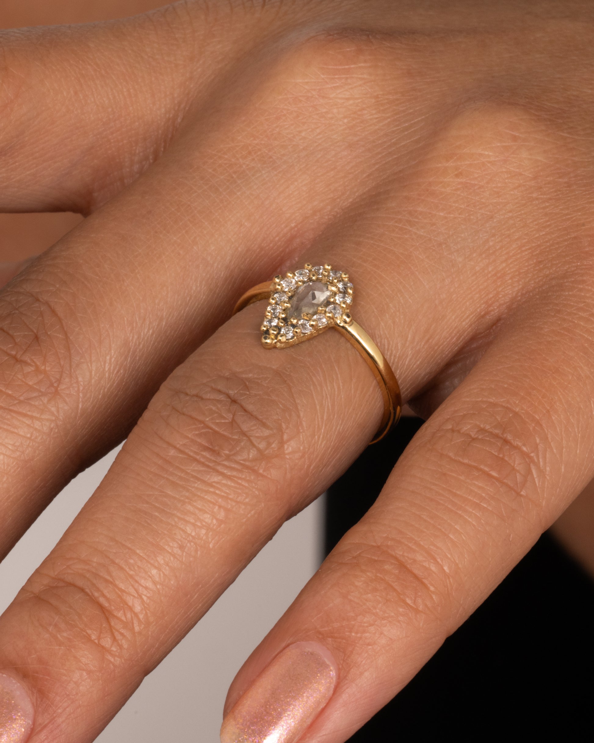 A light champagne, rose cut, pear shaped diamond ring with a round diamond halo. Shown worn on hand.