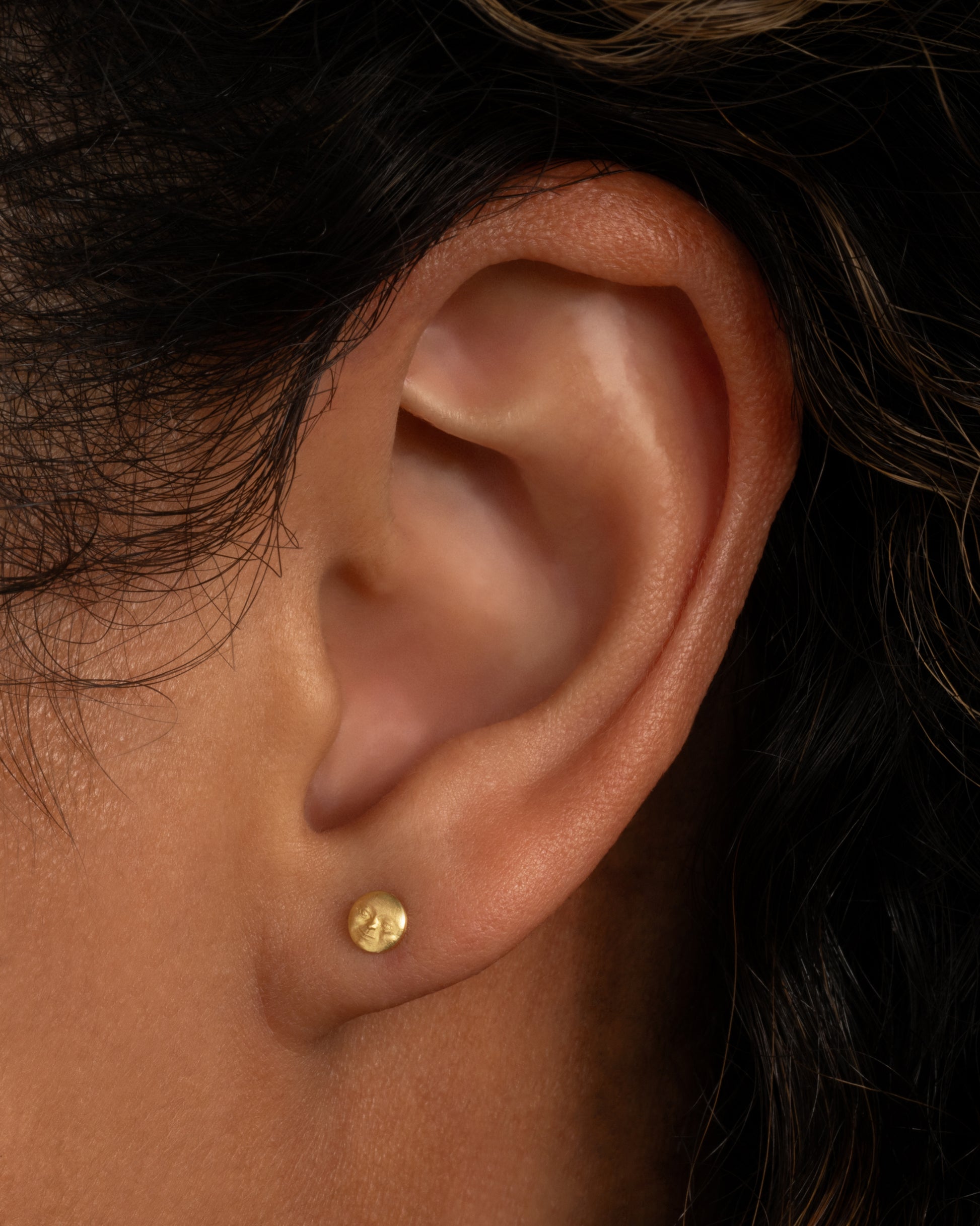 A yellow gold moon face stud earring. Shown from the side on a person.