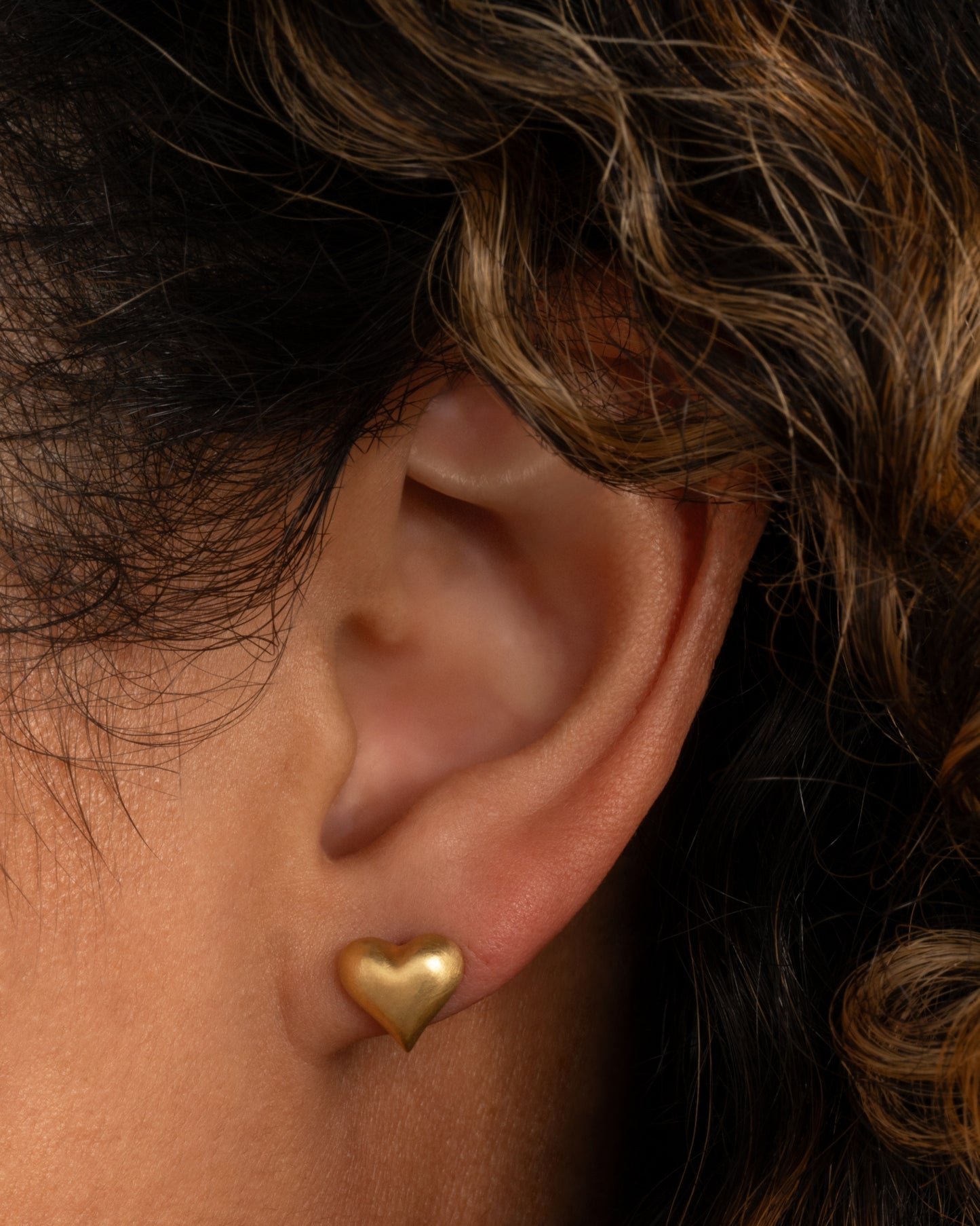 A yellow gold puffy heart stud earring. Shown worn in an ear.