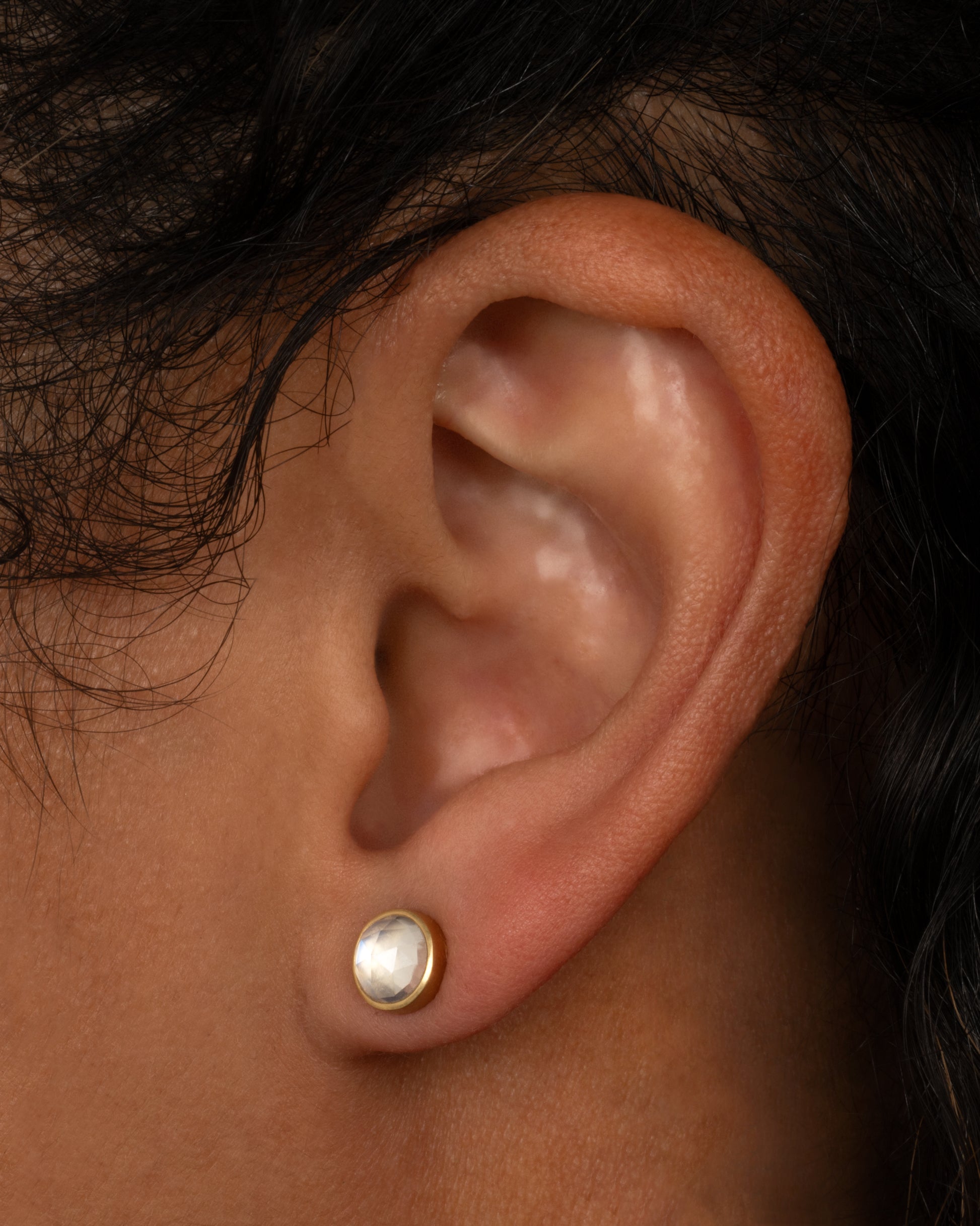 A yellow gold stud earring with a moonstone. Shown on an ear.