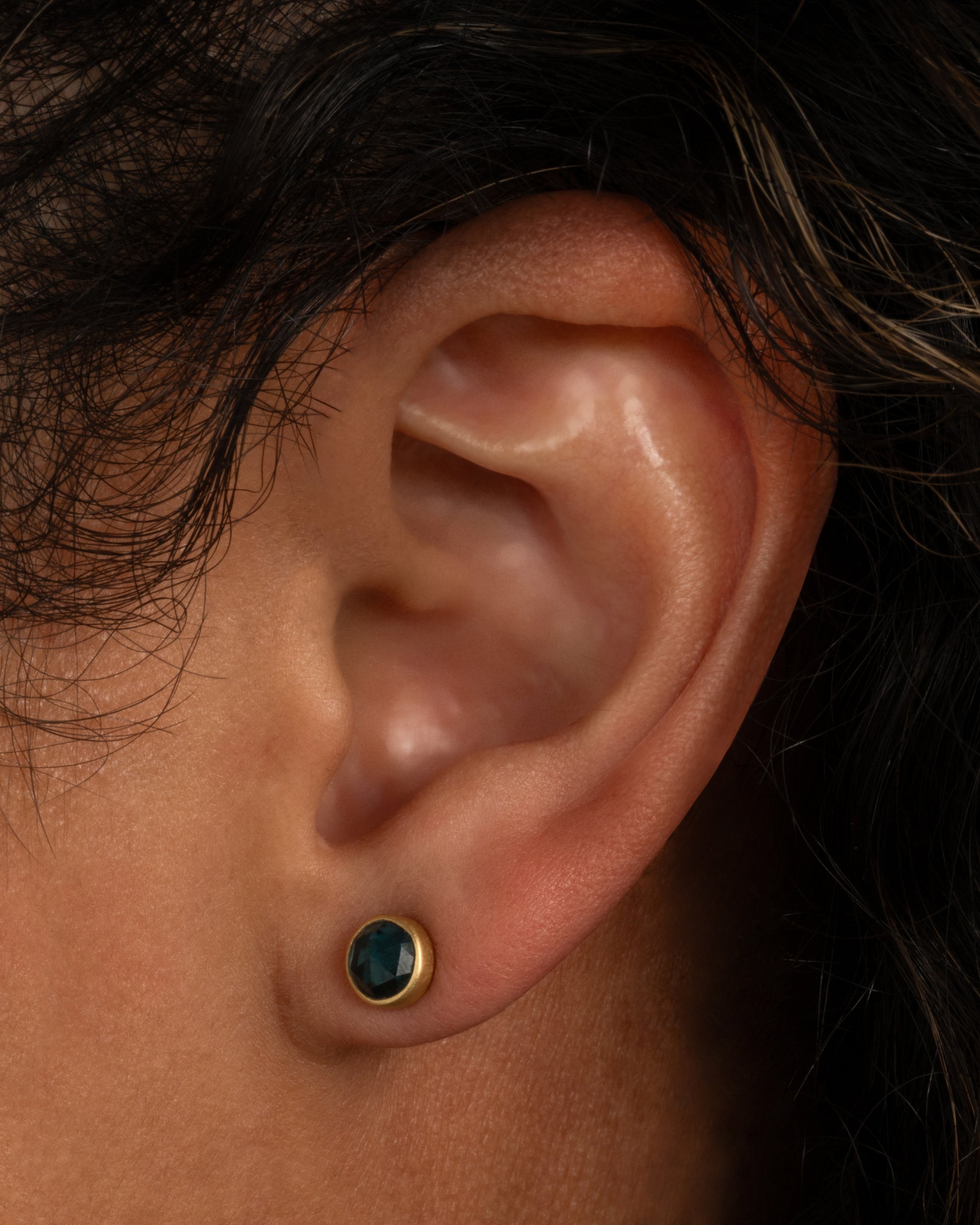 A yellow gold stud earring with a blue green tourmaline. Shown from the front on an ear.