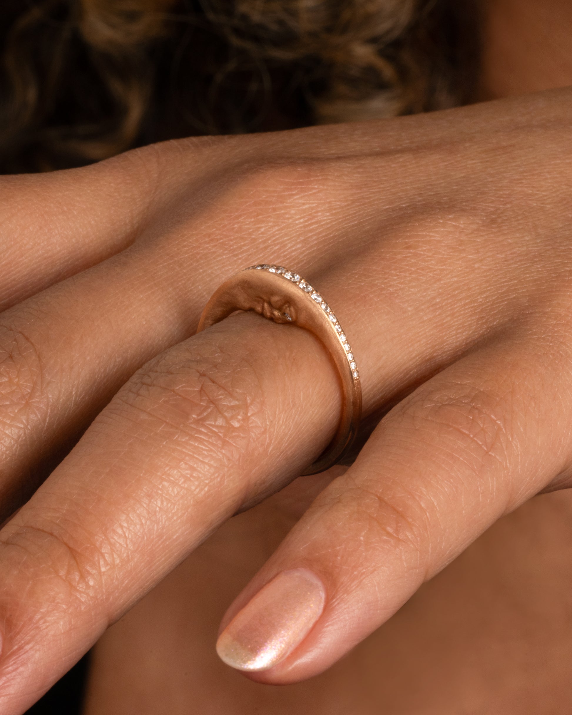 A rose gold crescent moon ring with a diamond eyed face and graduated white diamonds around the top edge. Shown worn on hand