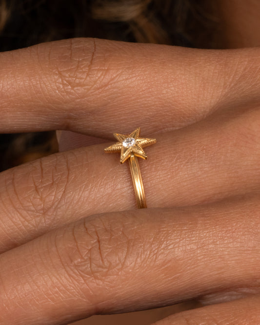An 18k gold six-point star ring with a round diamond nestled in the center shown worn on hand