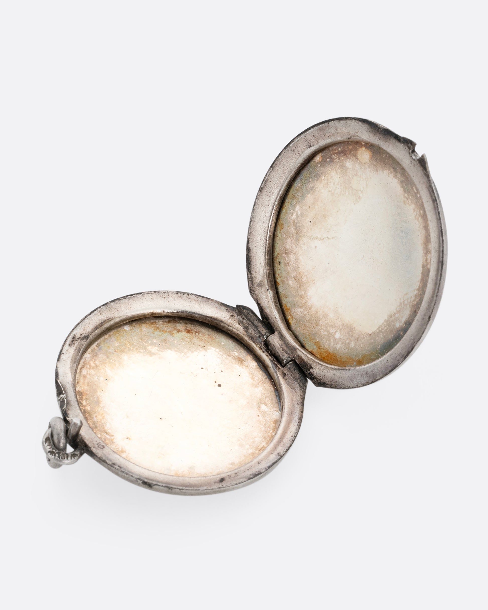 A circular silver locket shown open lying flat.