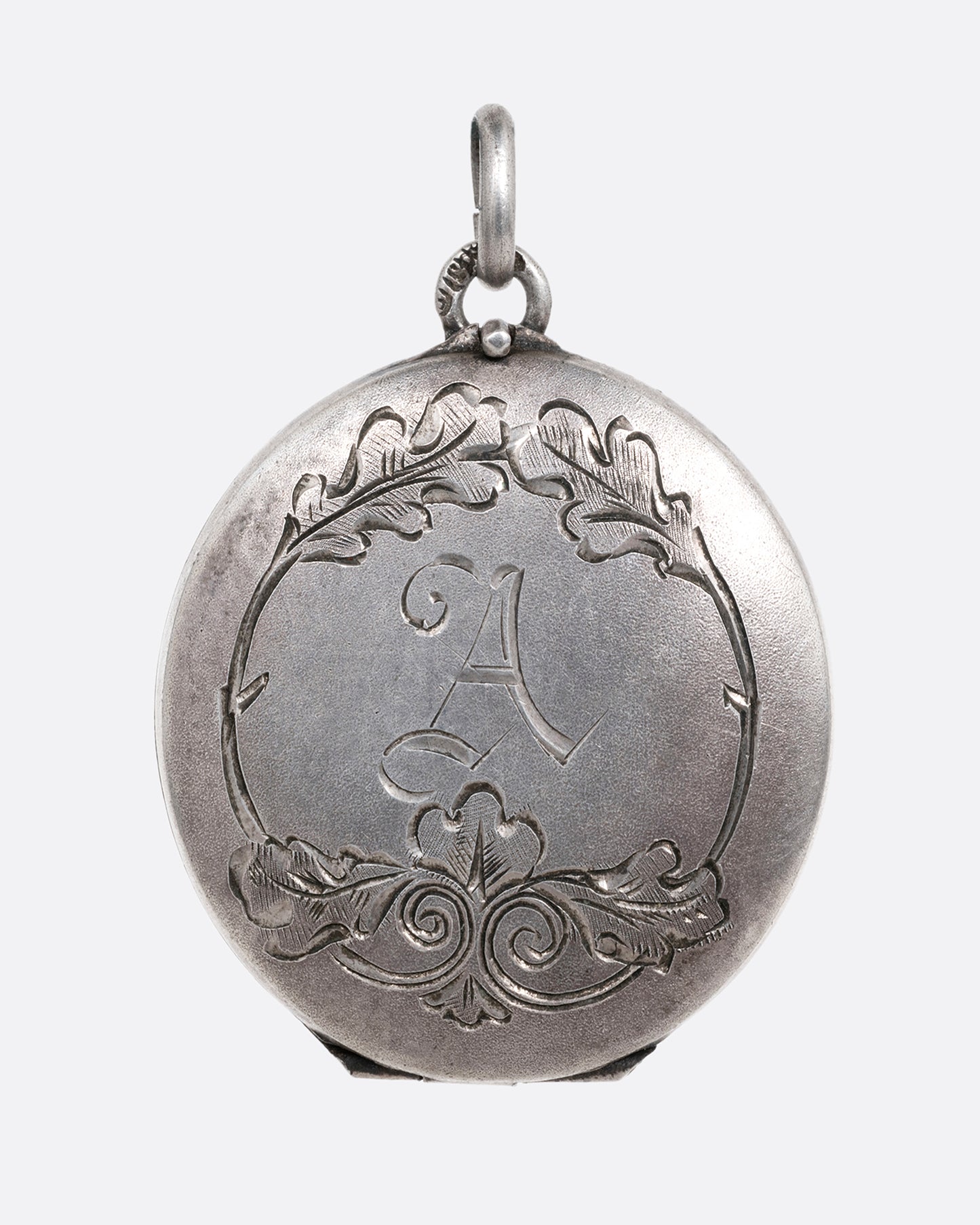 A silver locket with an engraved floral motif and an A' initial at the center. Shown from the front.