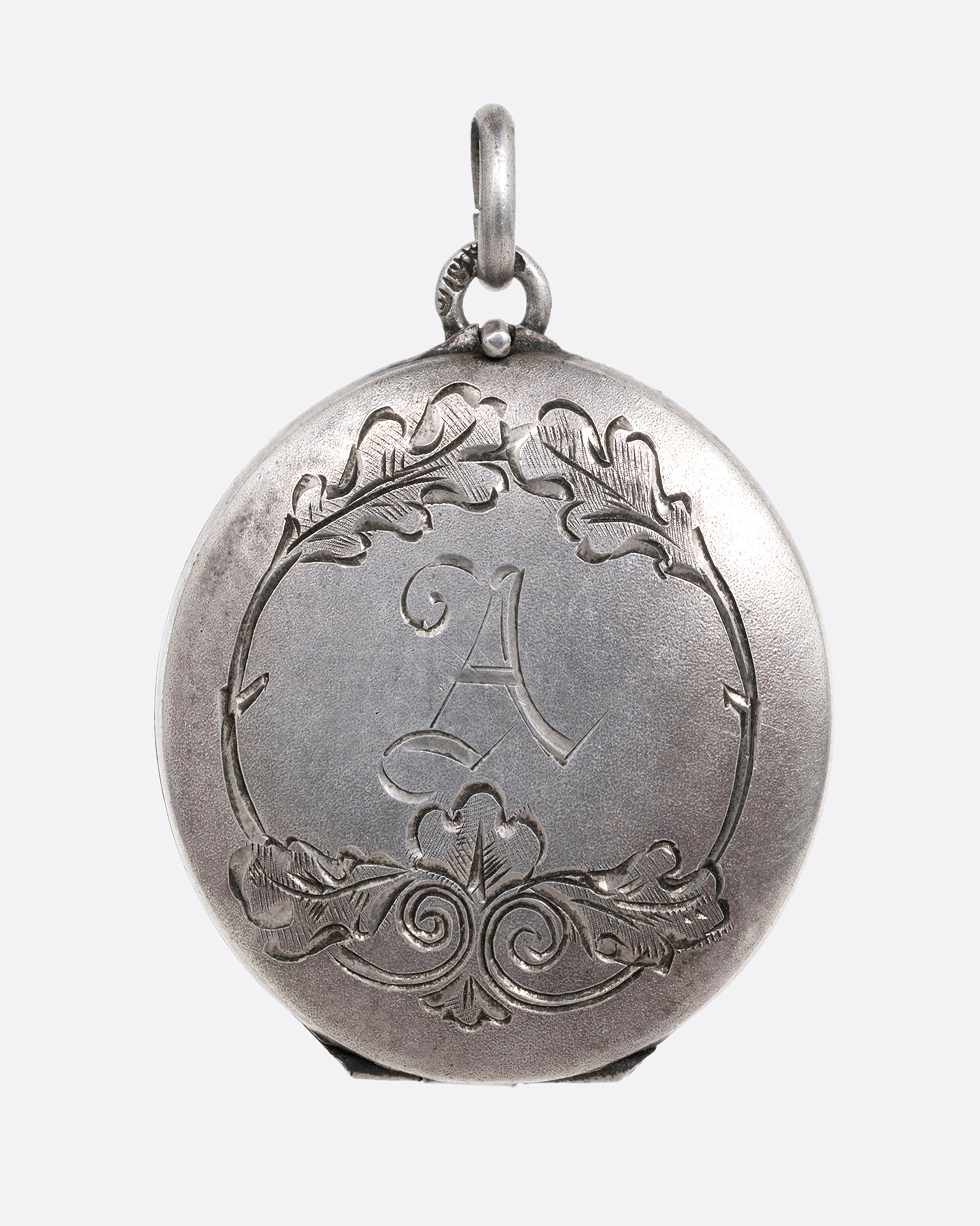 A silver locket with an engraved floral motif and an A' initial at the center. Shown from the front.