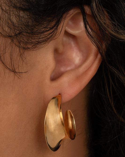A yellow gold hoop earring with a ribbon- like shape. Shown from the front on a person.