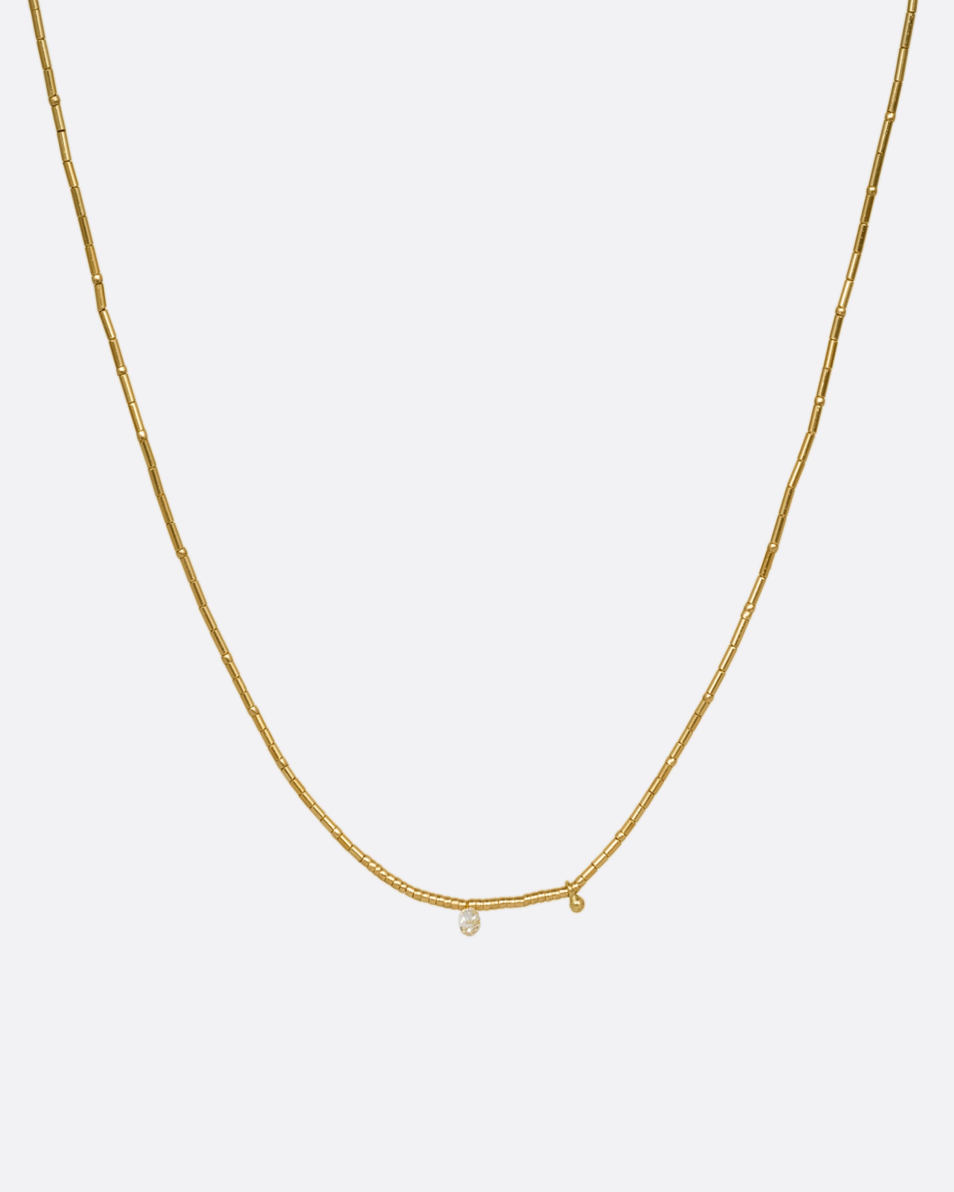 A yellow gold beaded necklace with a diamond briolette and pops of red cording beside the clasp. Shown from the front.