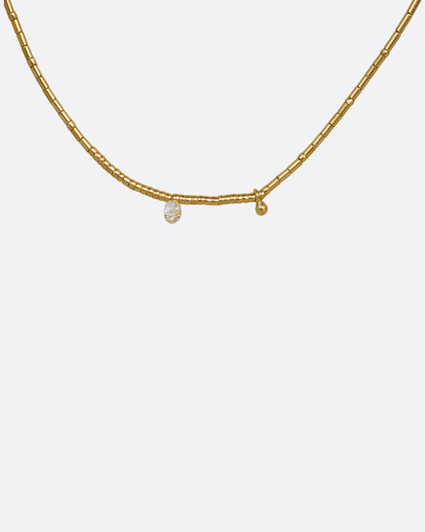 A yellow gold beaded necklace with a diamond briolette and pops of red cording beside the clasp. Shown from the front.
