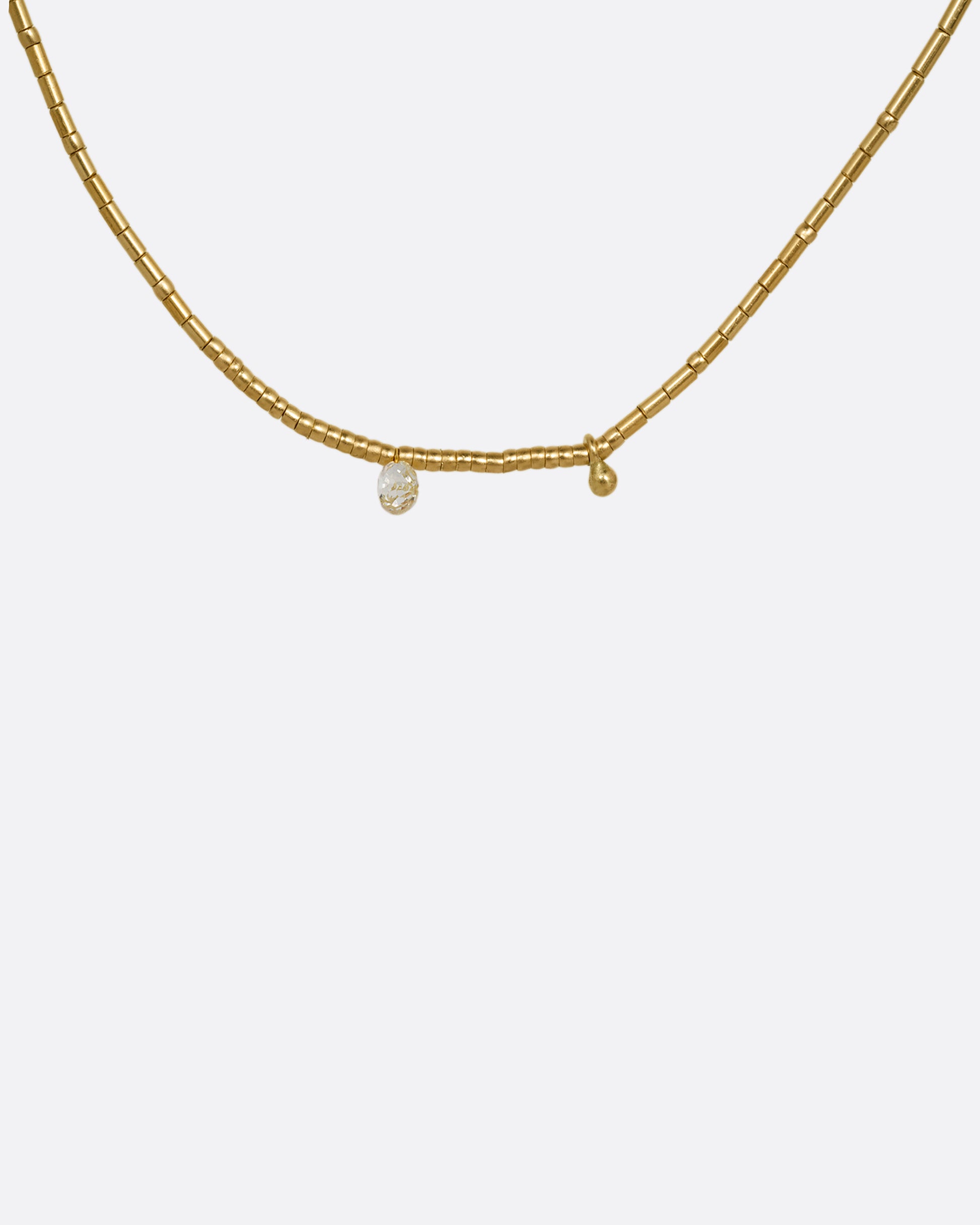 A yellow gold beaded necklace with a diamond briolette and pops of red cording beside the clasp. Shown from the front.