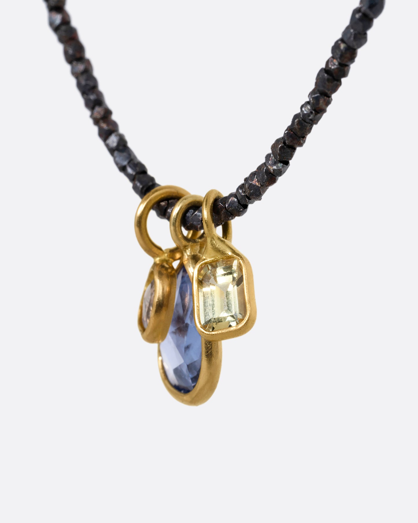A necklace with oxidized silver Hill Tribe beads and a cluster of blue and green sapphires and a rose cut diamond. Shown from the side.