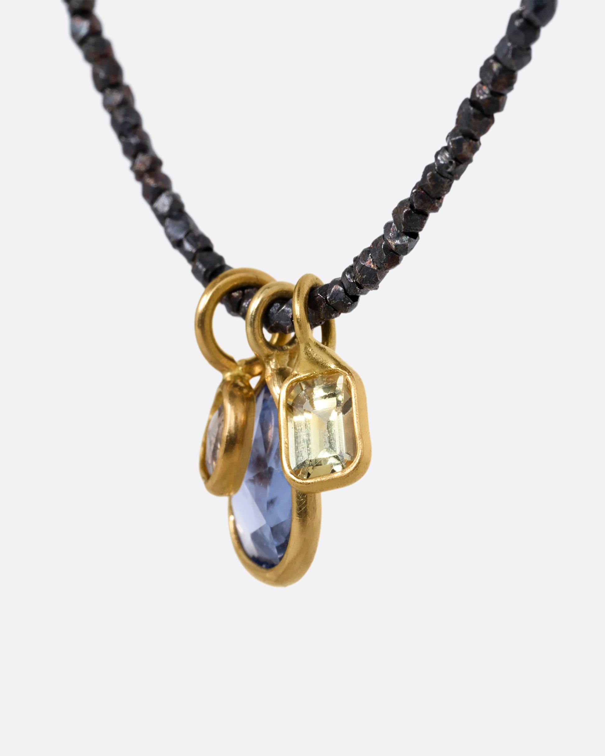 A necklace with oxidized silver Hill Tribe beads and a cluster of blue and green sapphires and a rose cut diamond. Shown from the side.