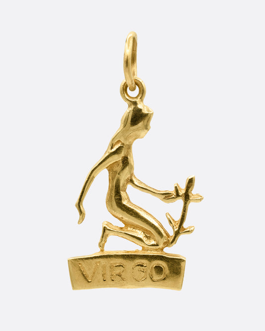 A yellow gold kneeling Virgo charm, depicted carrying a sheaf of wheat. Shown from the front.