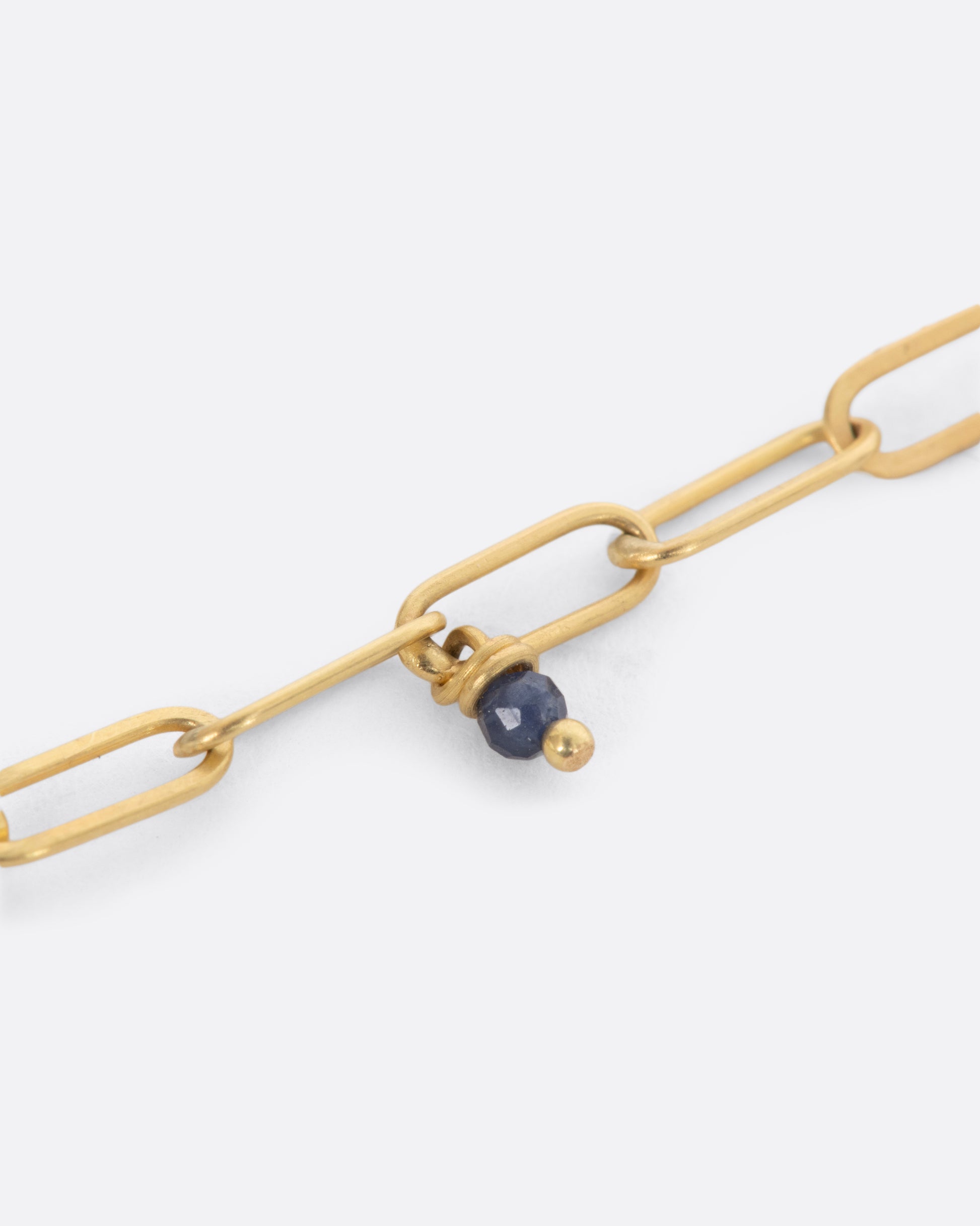 Yellow gold paper clip chain necklace with sapphire beads. View of the links and bead close up.