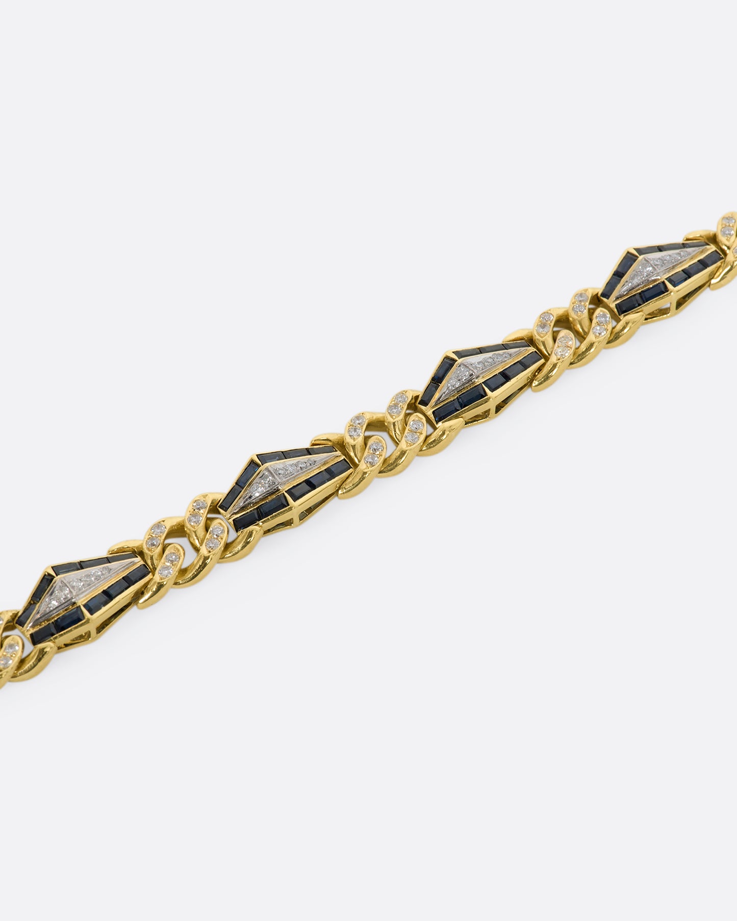 Yellow gold curb chain bracelet with sapphire baguette stations and diamonds throughout. View from above laying flat.