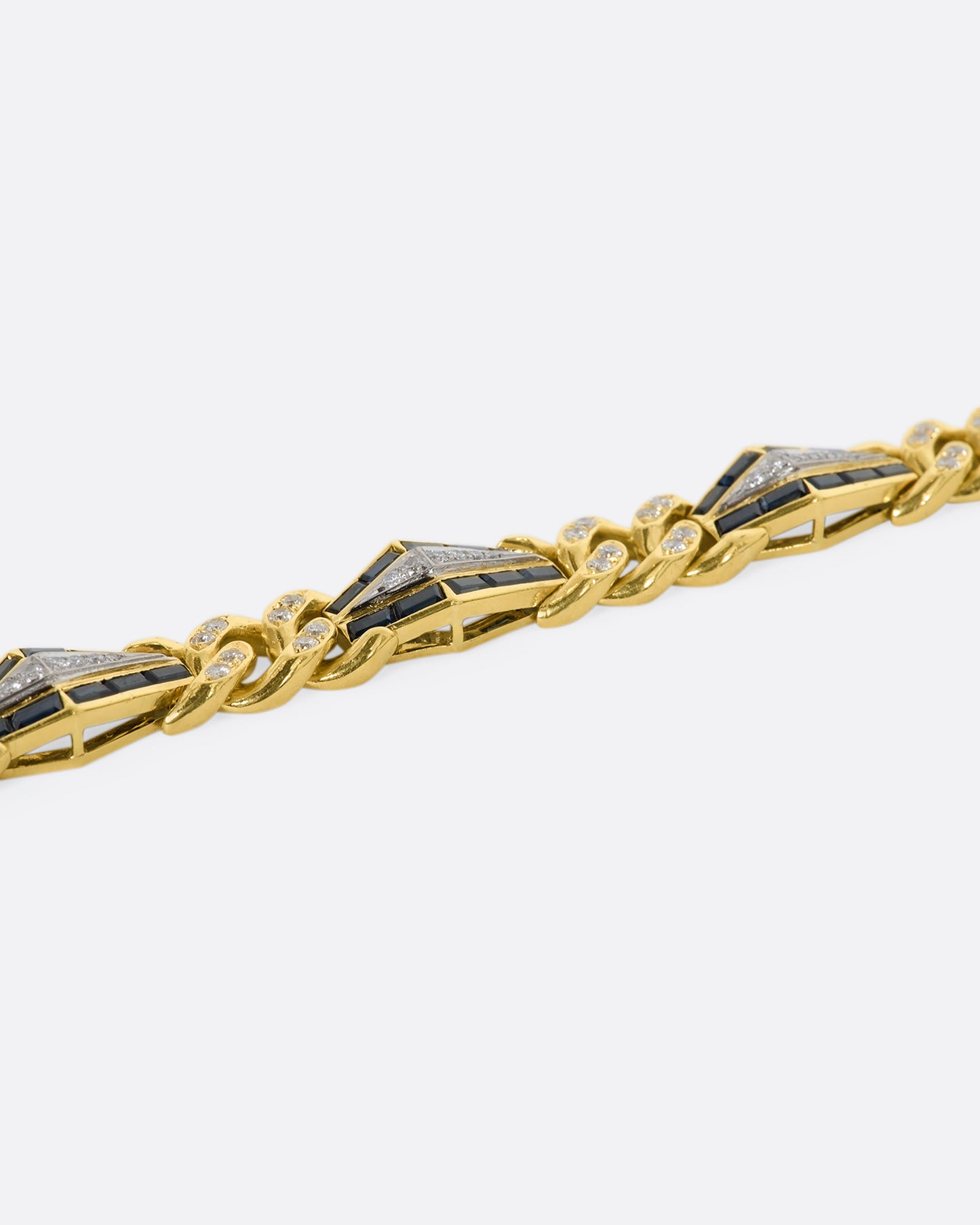 Yellow gold curb chain bracelet with sapphire baguette stations and diamonds throughout. View from the side.