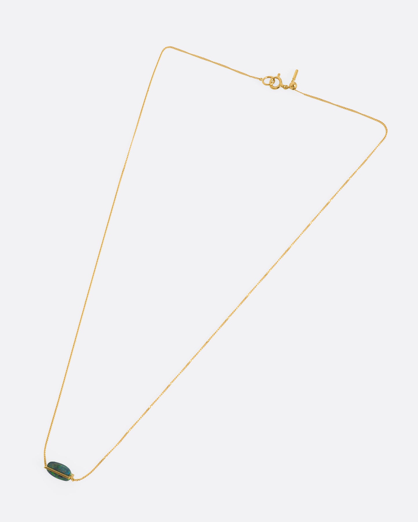 A yellow gold necklace with an oval black opal. View from above, laying flat.