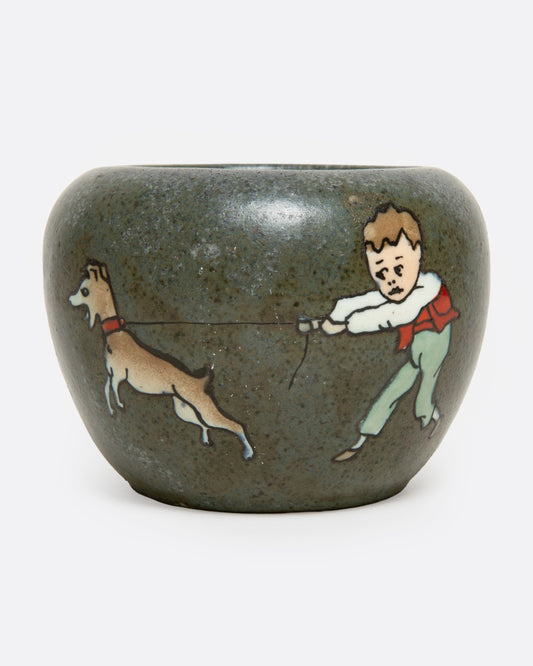 A ceramic vase with a handpainted image of a dog and boy, shown from the front.