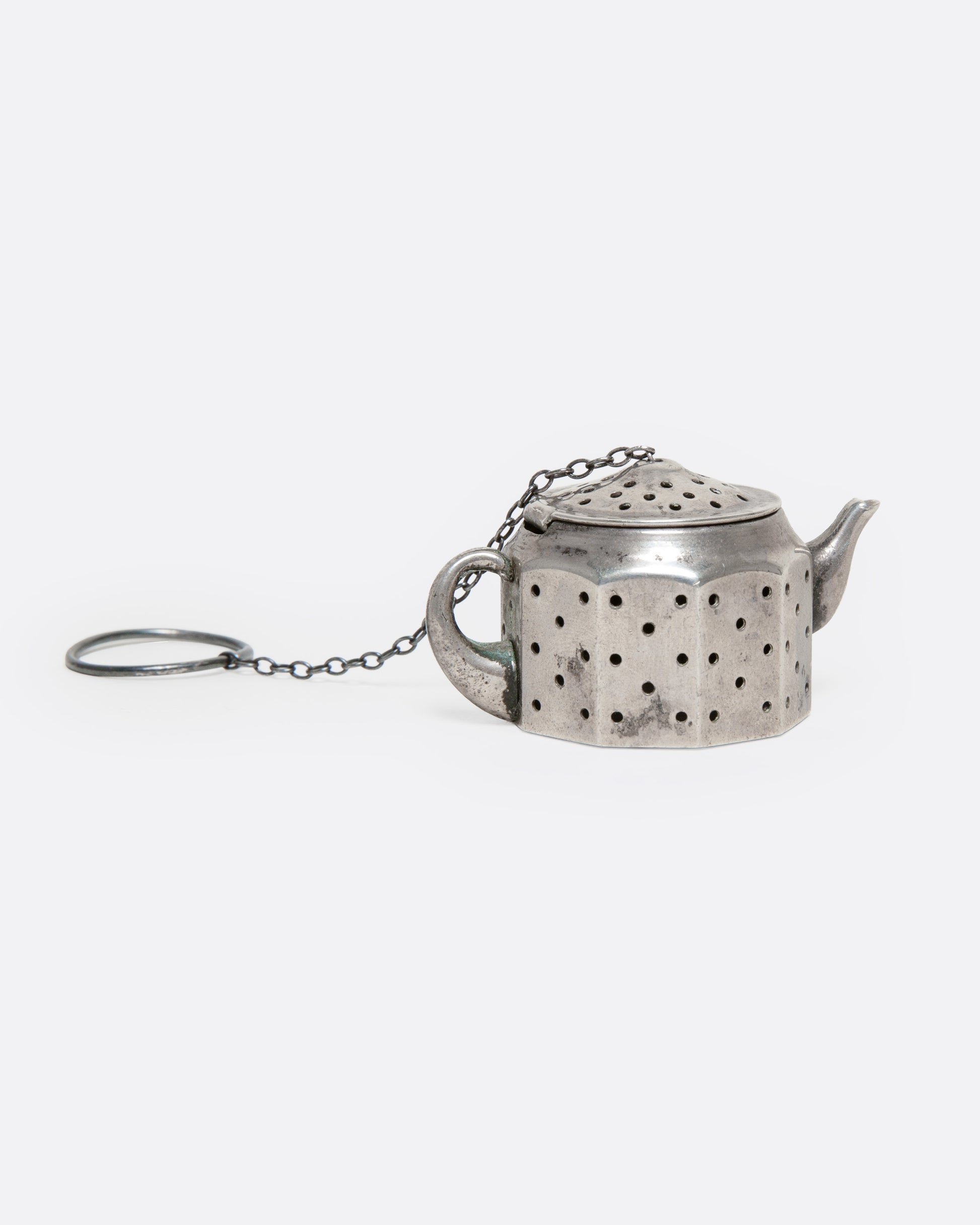 A silver teapot shaped infuser, topped with a hinged lid, shown from the side.