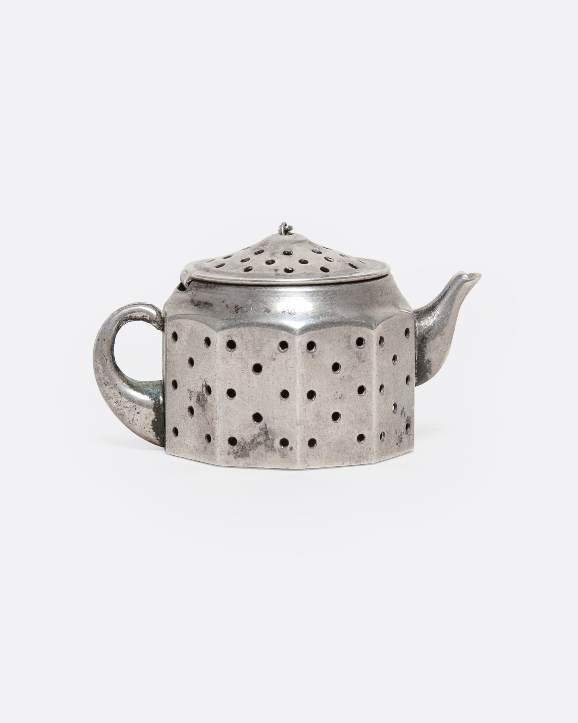 A silver teapot shaped infuser, topped with a hinged lid, shown from the side.