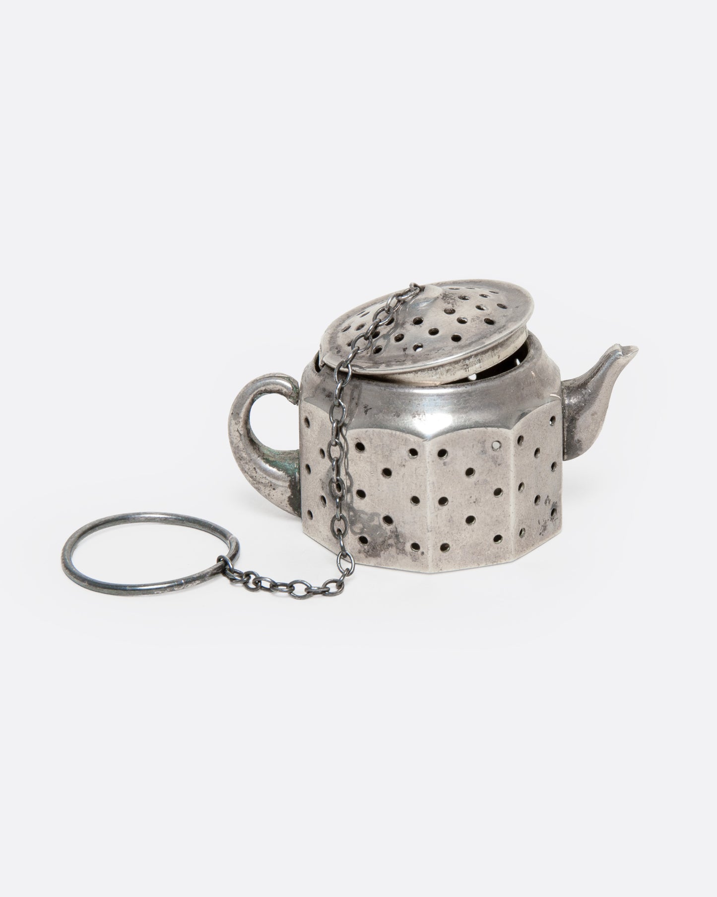 A silver teapot shaped infuser, topped with a hinged lid, shown from the side.