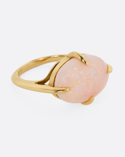 A yellow gold ring with a prong set opal, shown from the side.