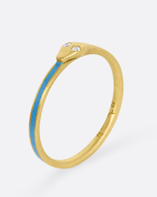 A yellow gold ouroboros ring with diamond eyes and pale blue enamel, shown standing up from the side. 