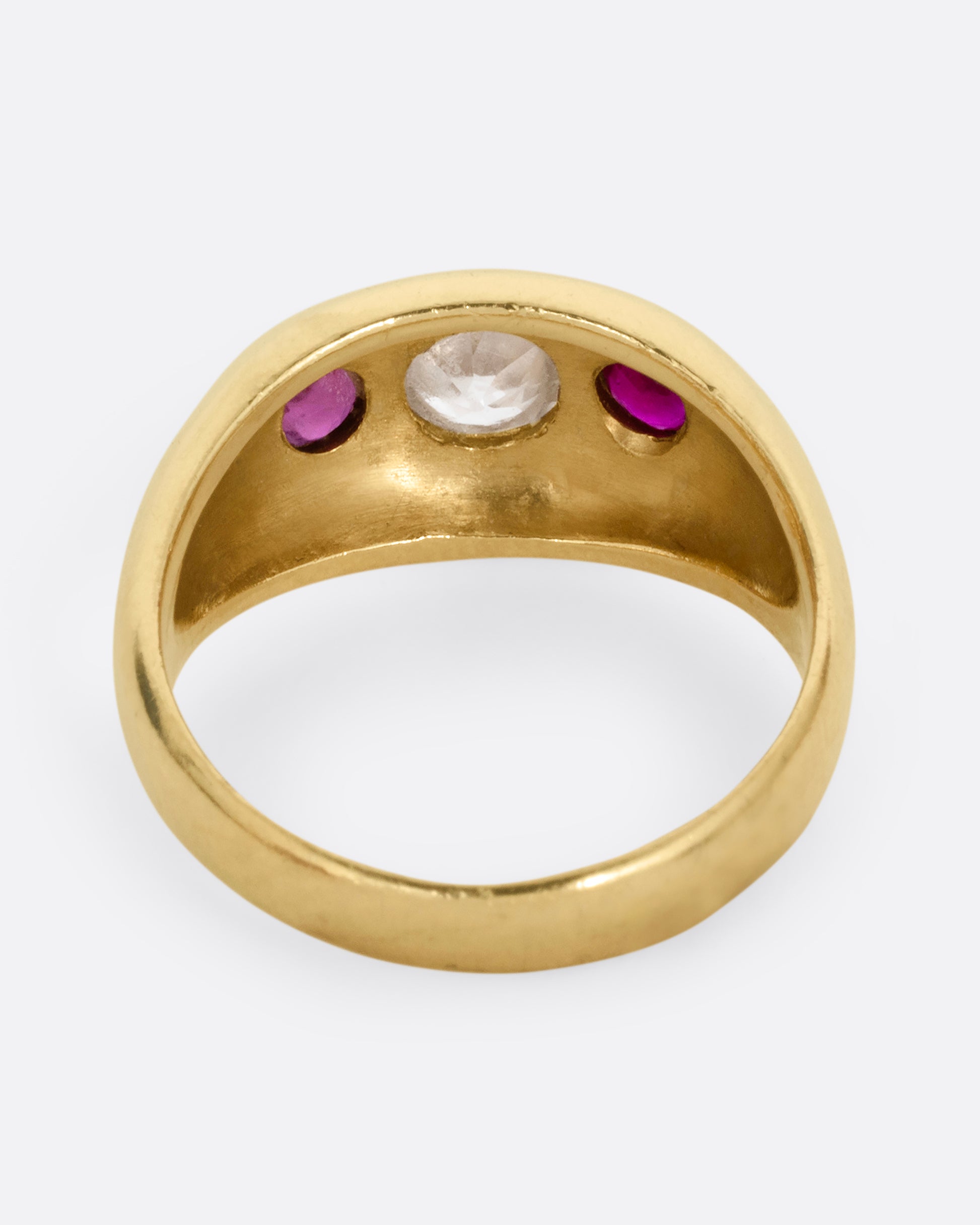 A yellow gold dome ring with a central diamond flanked by two rubies. Shown from the back.