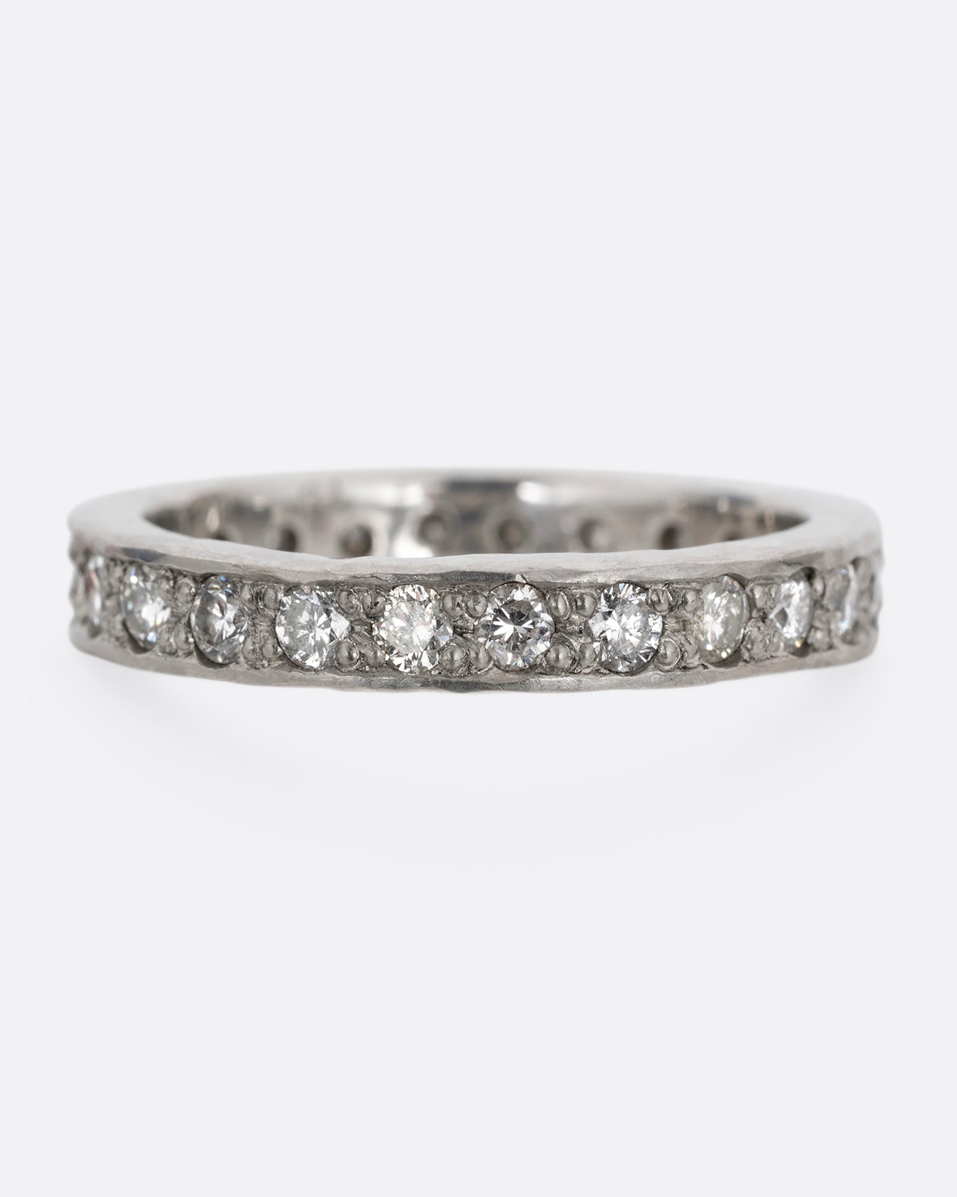 A platinum band with hammered edges and a darkened center with diamonds throughout. Shown from the front.