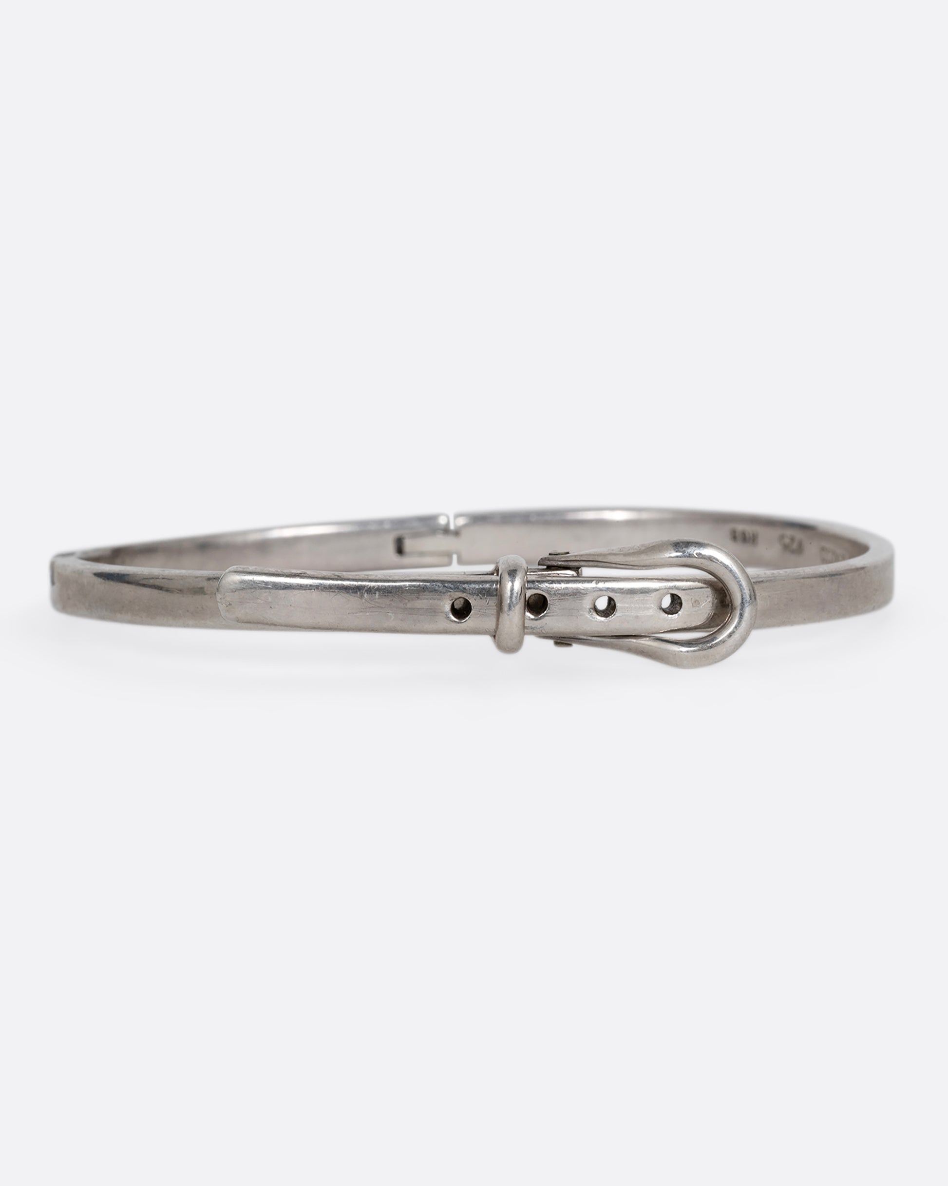 A narrow silver hinged bracelet with a buckle front. Shown from the front.