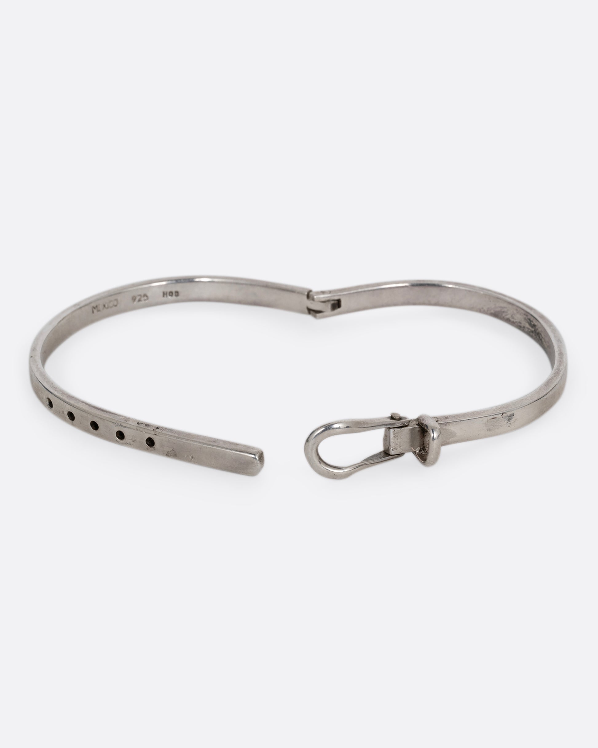 A narrow silver hinged bracelet with a buckle front. Shown open from the front.