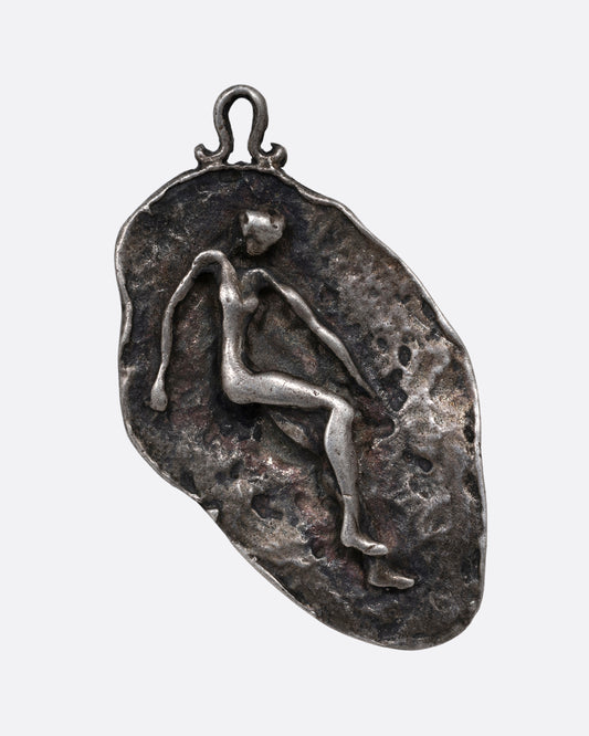 A silver freeform pendant with a figure emerging from a textural background. Shown from the front.