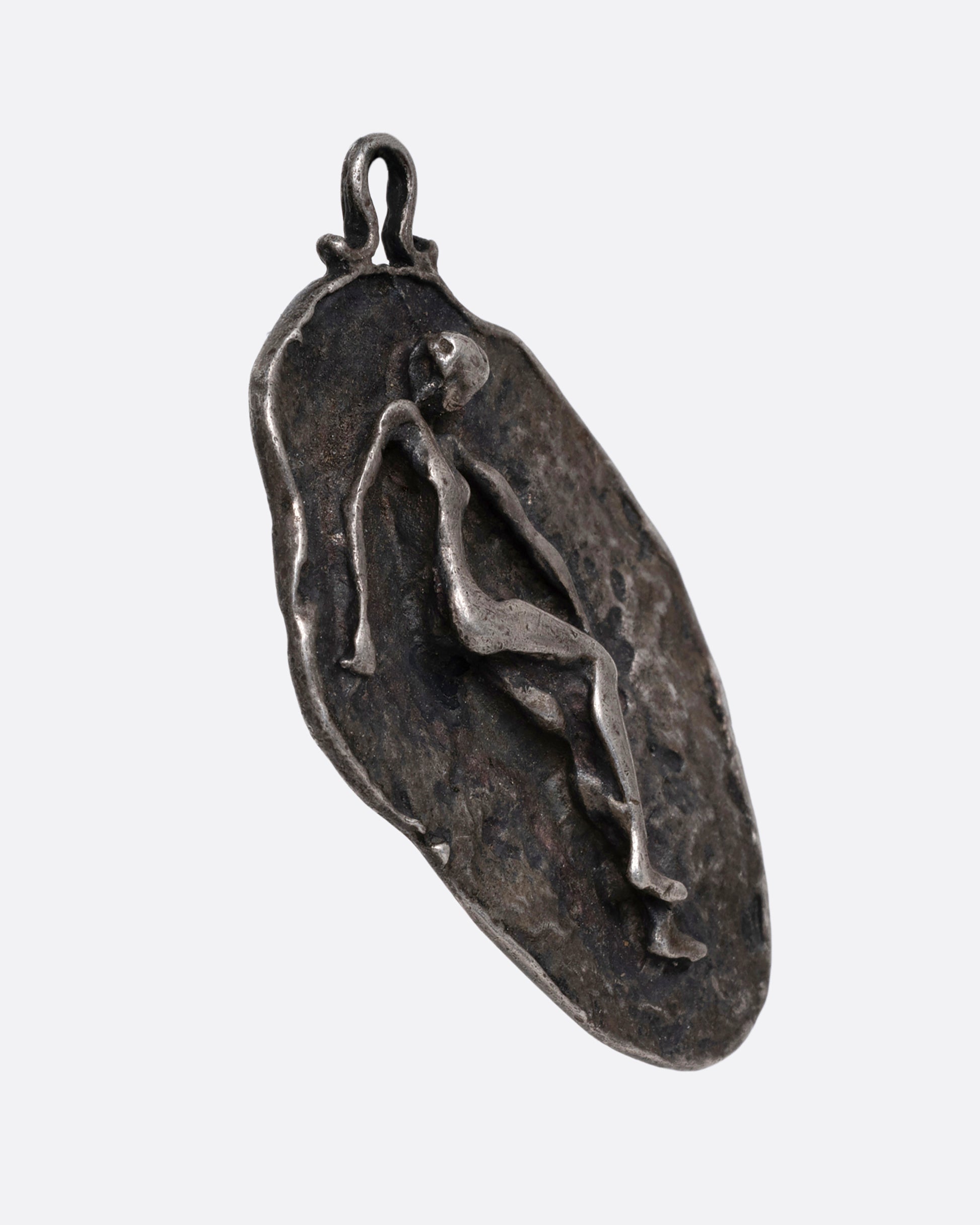 A silver freeform pendant with a figure emerging from a textural background. Shown from the side.