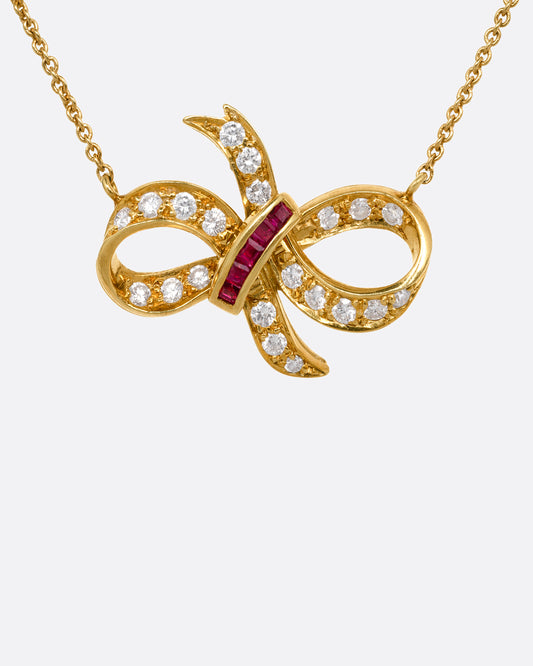 A yellow gold cable chain necklace with a diamond and ruby studded bow at the center. Shown from the front.