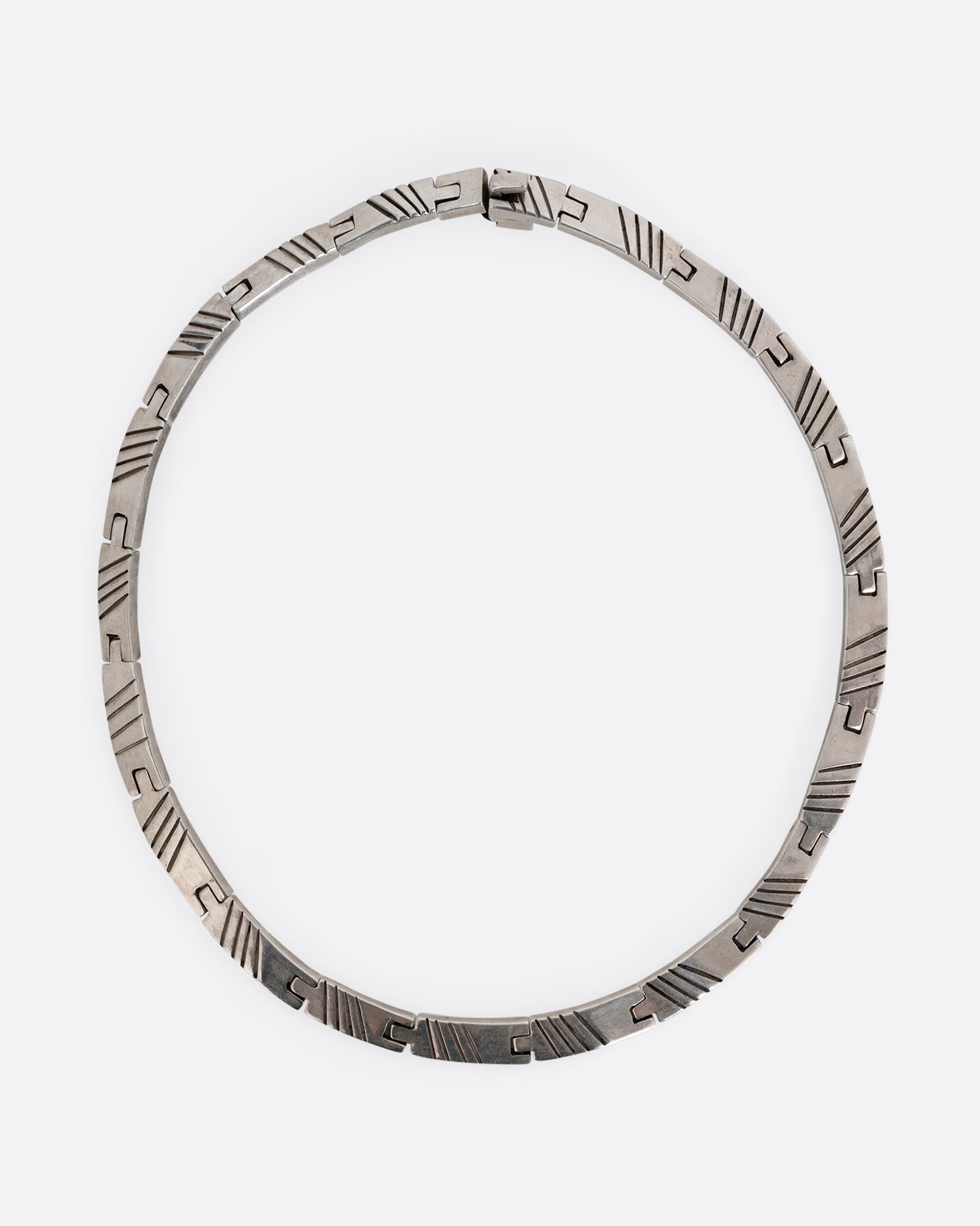 A silver collar necklace with hinged rectangular links and striped etchings. Shown from the top.