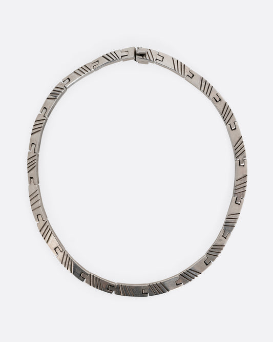 A silver collar necklace with hinged rectangular links and striped etchings. Shown from the top.