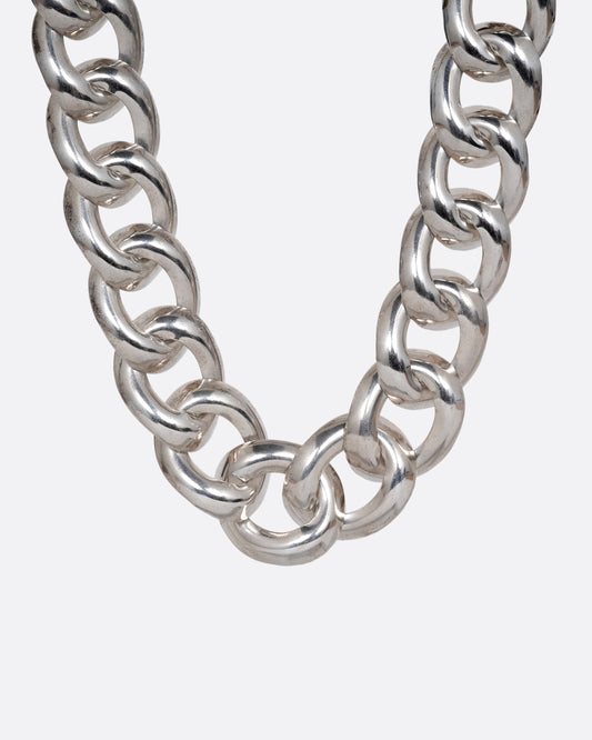 A silver curb chain necklace with a wide silhouette. Shown from the front.