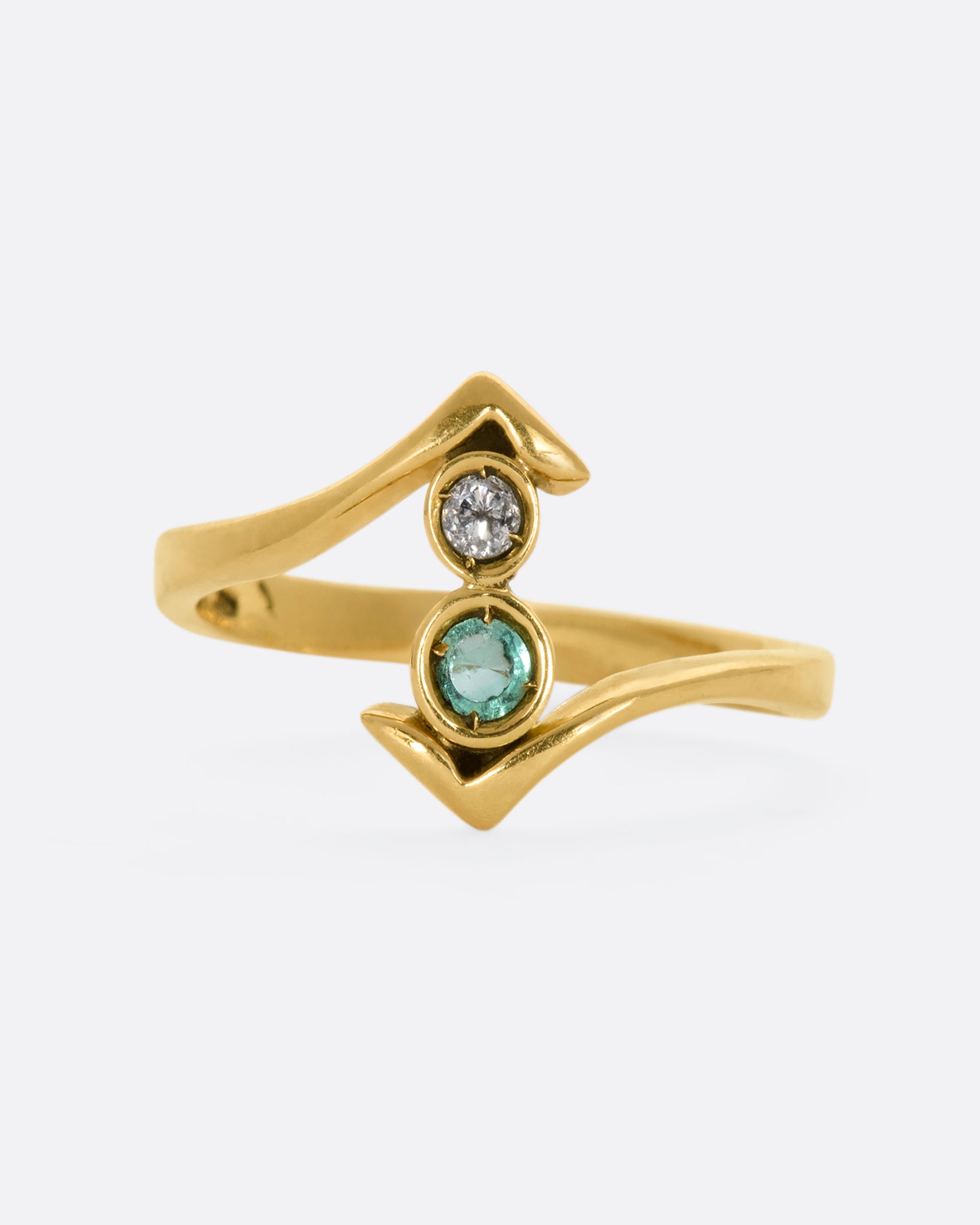 A yellow gold wrap ring with a round diamond and emerald. View close up from the front.