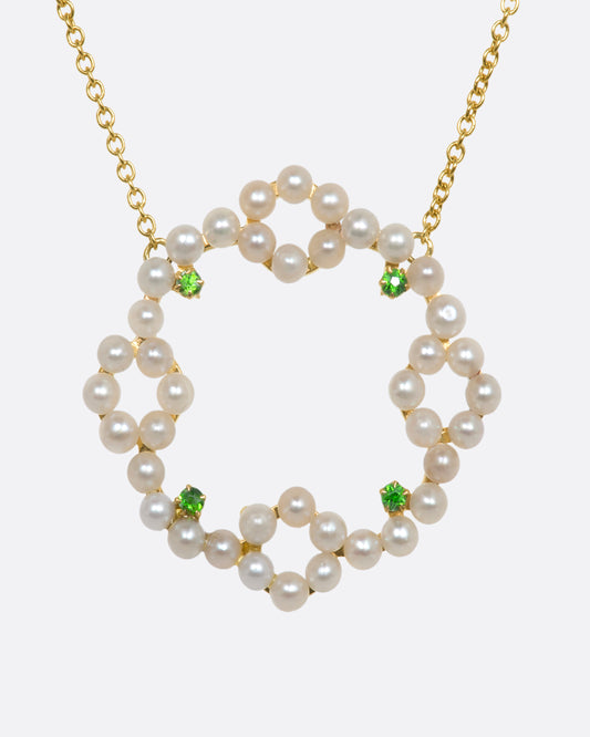 A yellow gold necklace with a pearl and green garnet wreath pendant. View from the front.