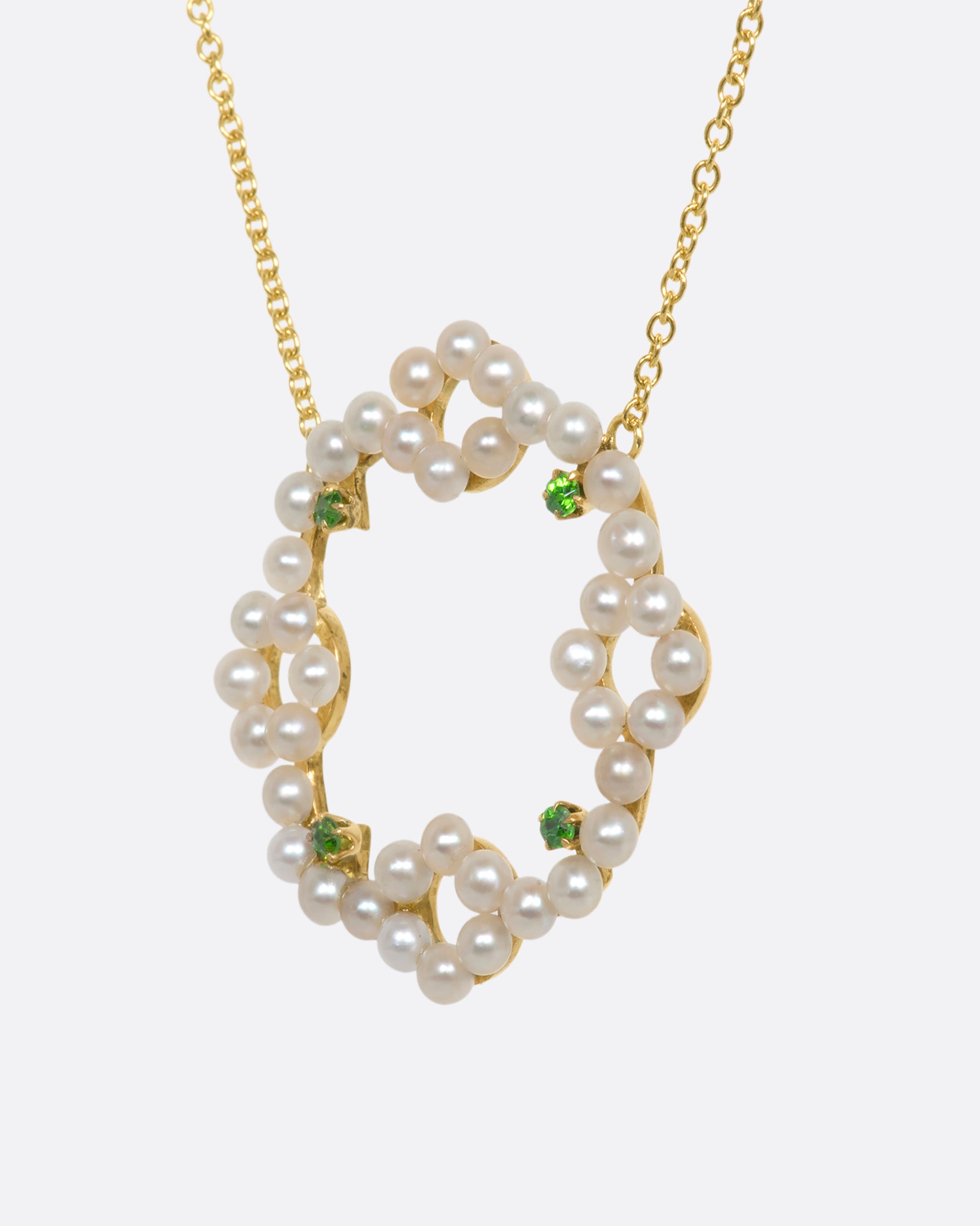 A yellow gold necklace with a pearl and green garnet wreath pendant. View from the side.