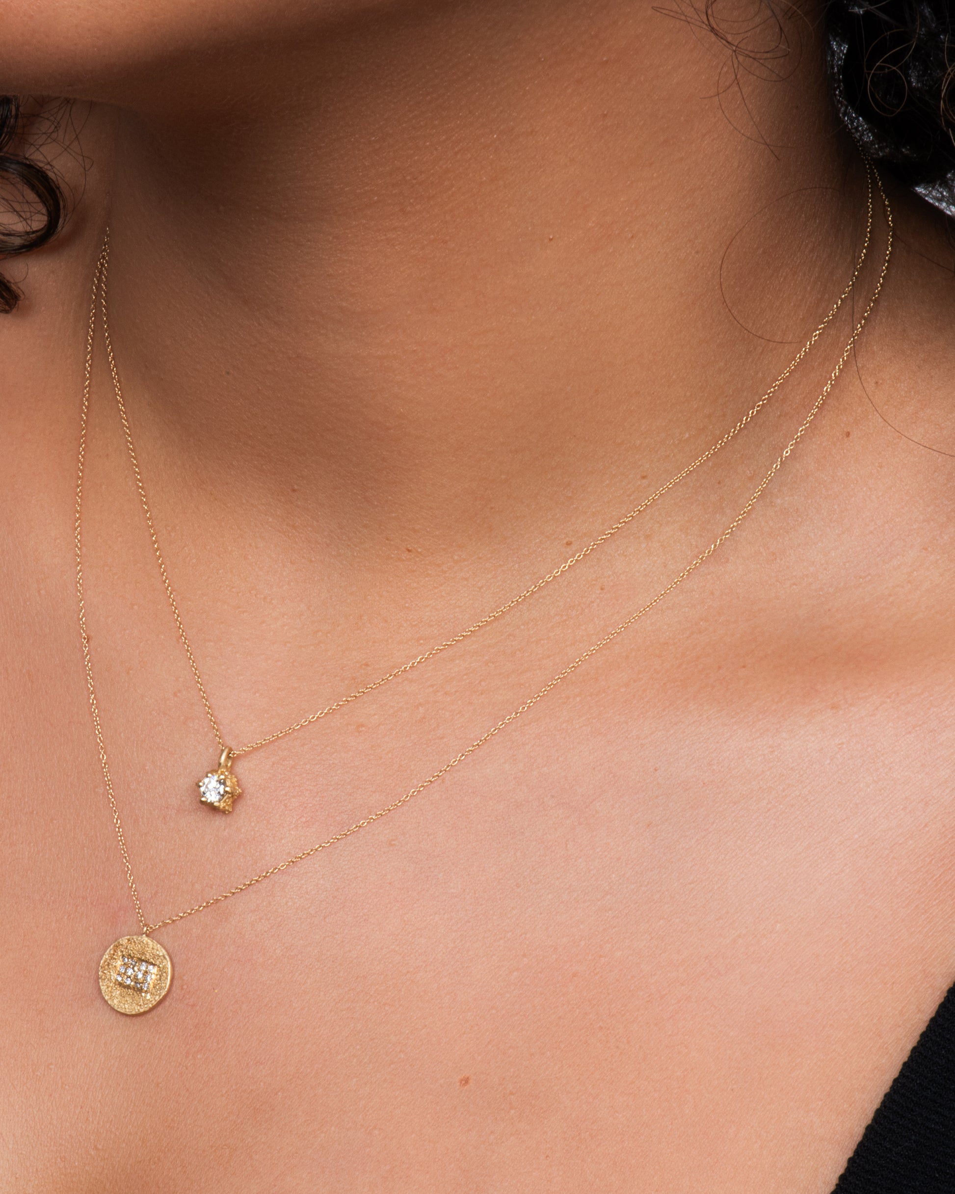 Yellow gold necklace with solitaire diamond in a textured prong setting. Shown on a neck paired with a diamond disk pendant from the same designer.