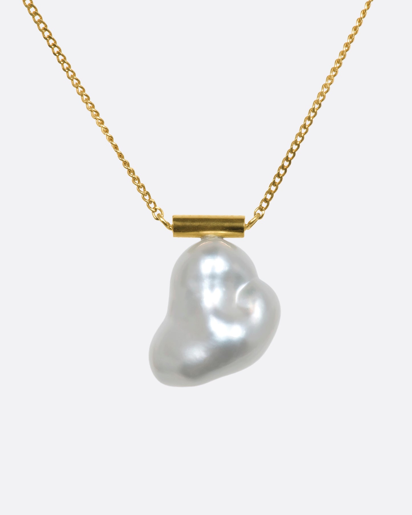 A freeform South Sea baroque pearl is suspended from a minimalist gold bar and fine yellow gold cable chain. The beautiful, natural curvature of this rare pearl allows light to reflect in a multitude of paths, glowing from every angle.