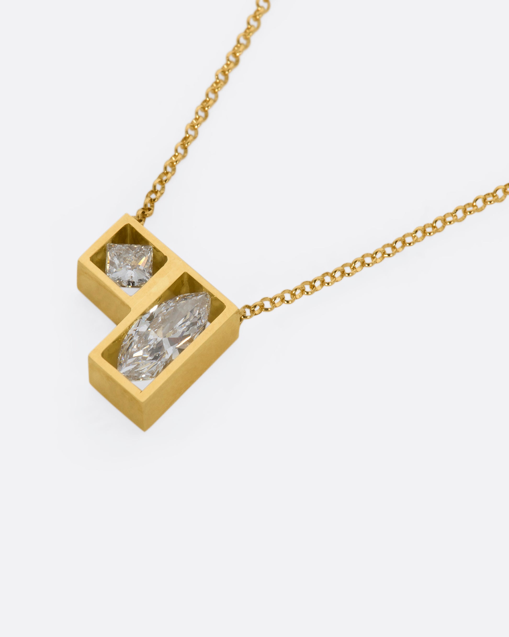 A yellow gold square and rectangle frame fixed pendant hold a marquise and a princess cut diamond hanging from a chain. View laying flat.